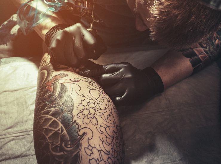 Tatuatore mentre fa un tatuaggio su di un polpaccio