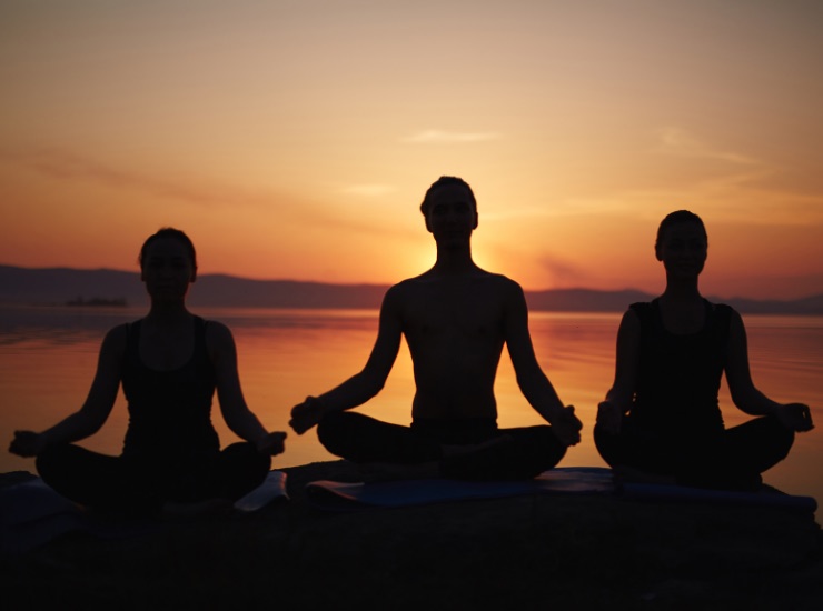 Tre figure fanno meditazione yoga al tramonto