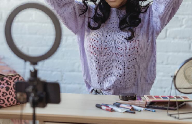 Una ragazza sopra a un banco di lavoro con tanti accessori delmondo del beauty e una ring-light per registrare contenuti 