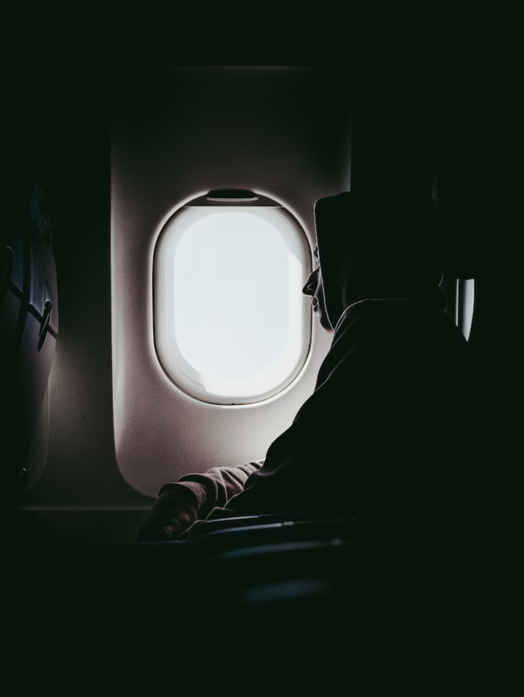 uomo col cappuccio appoggiato al finestrino dell'aereo