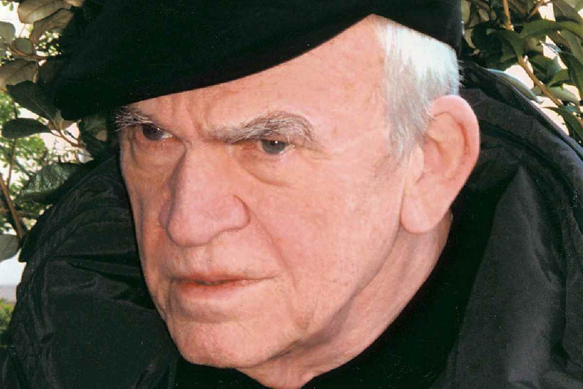 Milan Kundera da anziano con un berretto e una espressione corrucciata che guarda a sinistra in basso
