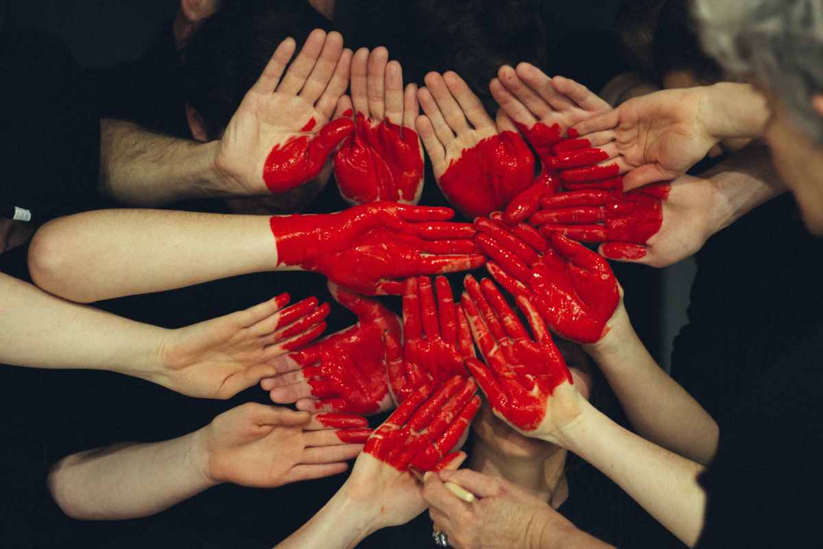Tante mani insieme dipinte di rosso che formano un cuore